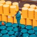 Worker inspecting stacked chemical storage drums.