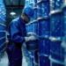 Worker inspecting methacrylic acid drums in industrial storage.